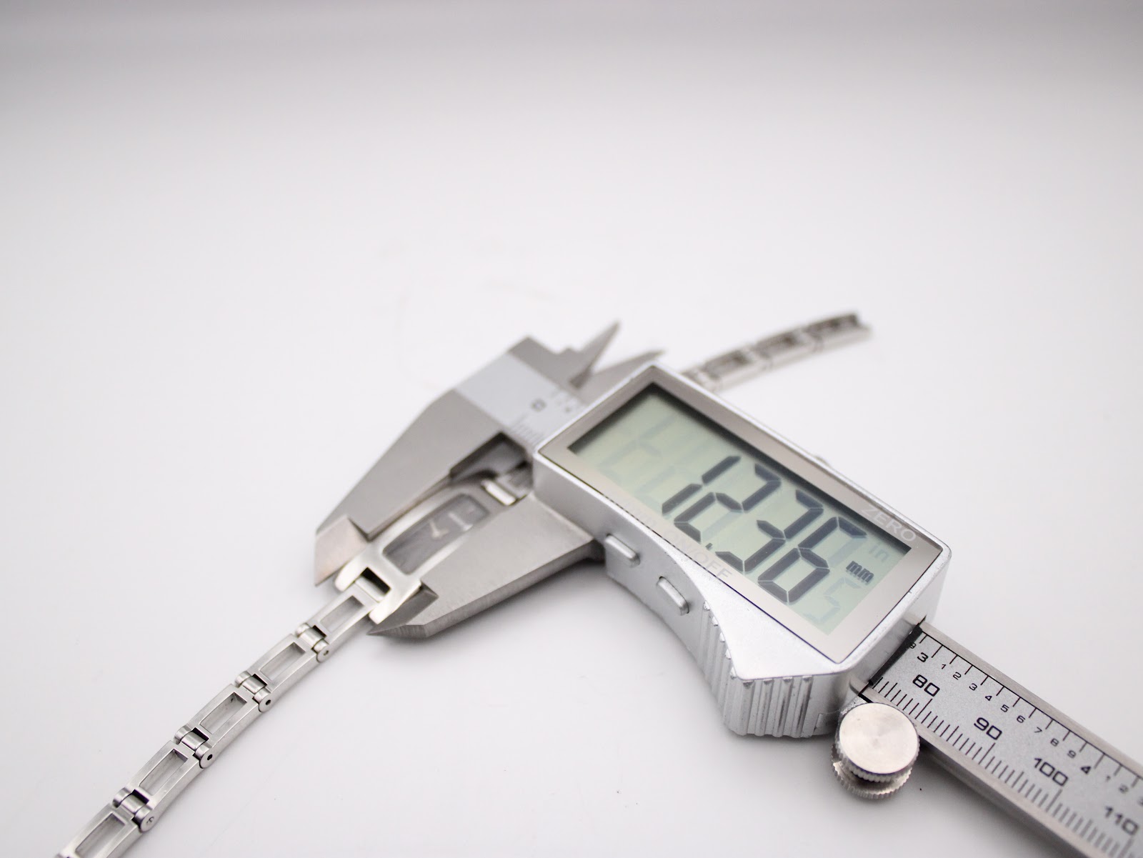 Close-up of a digital caliper measuring a link of the Gucci 3900L's bracelet, showing a width of 12.36mm.