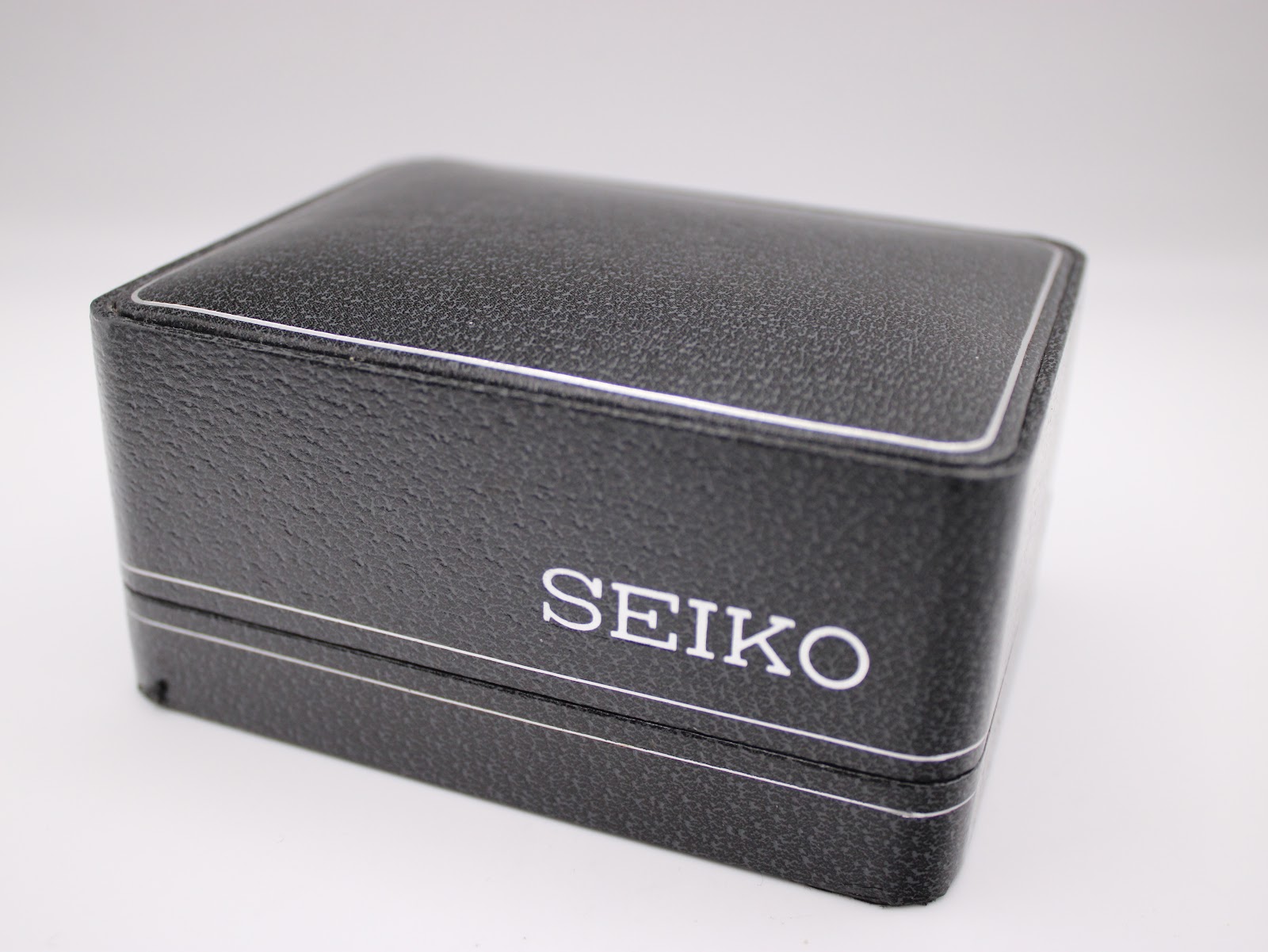 Original black textured Seiko watch box with white 'SEIKO' logo, closed.