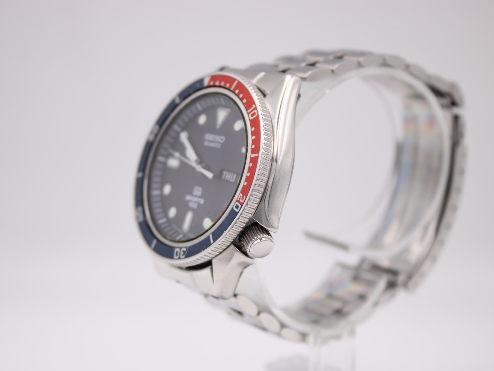Right profile view of the Seiko diver watch on a clear display stand, showing the crown and knurled bezel edge.