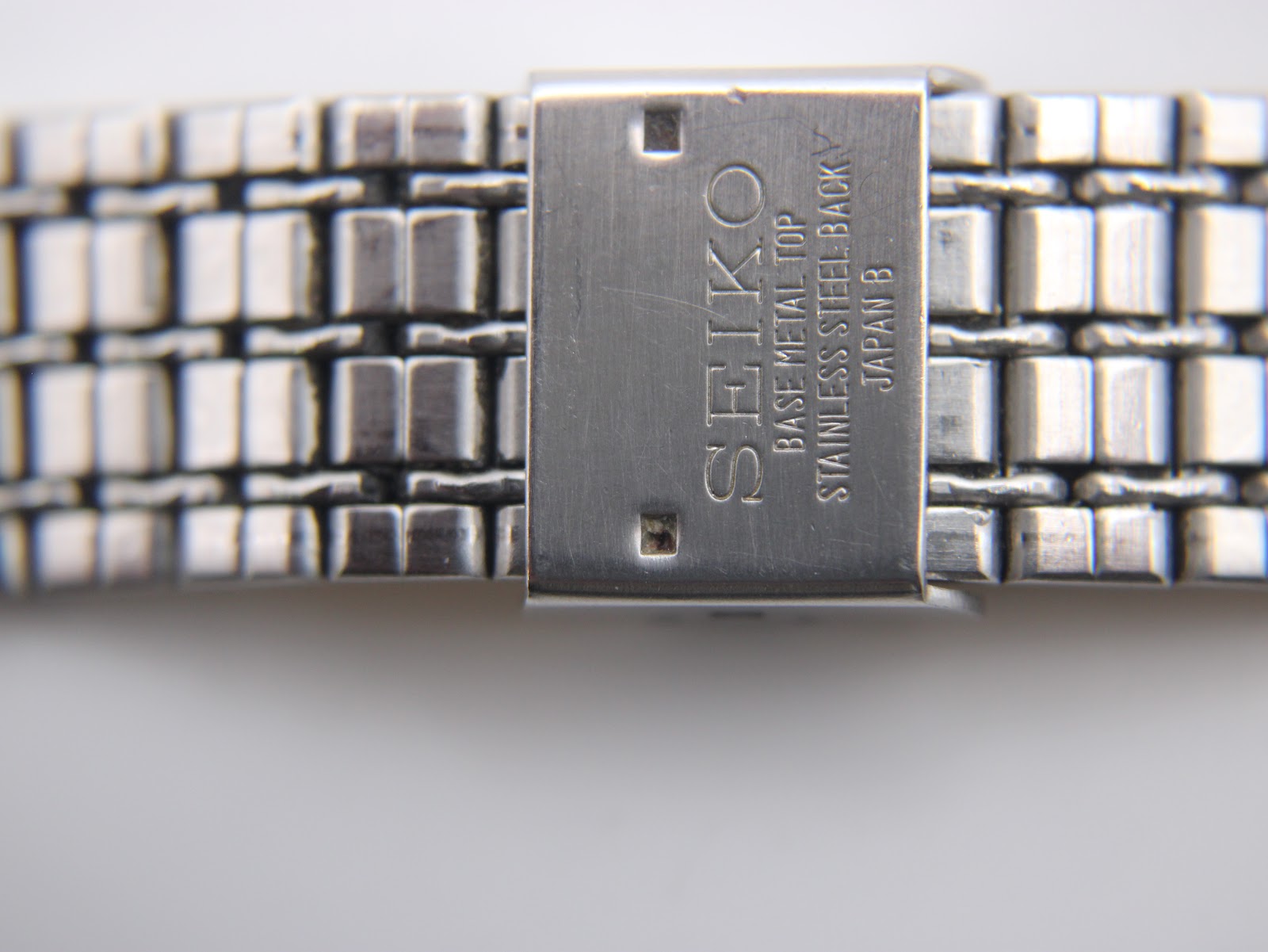 Close-up of the gold tone integrated bracelet clasp, showing the 'SEIKO' signature and 'BASE METAL TOP ST. STEEL BACK' markings.