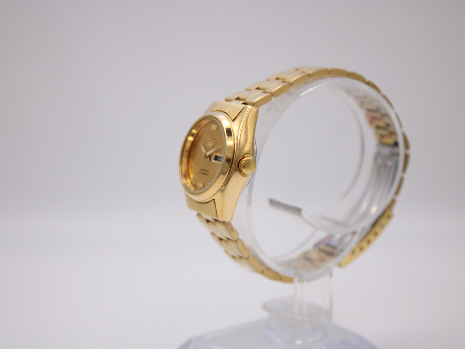 Side view of gold tone Seiko automatic watch on a clear stand, showing the crown.