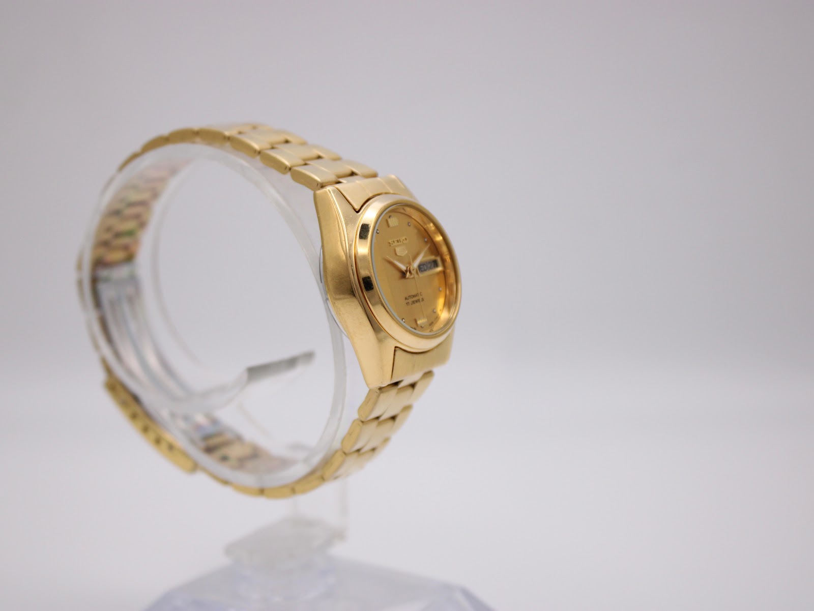 Other side view of gold tone Seiko automatic watch on a clear stand, showing bracelet links.
