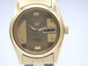 Close-up of the gold dial of the Seiko watch, showing day-date window with Arabic and English script, 'Automatic 17 jewels' text.