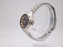 Side profile view of the Seiko watch, showing the gold-tone crown and fluted bezel detail on a clear stand.