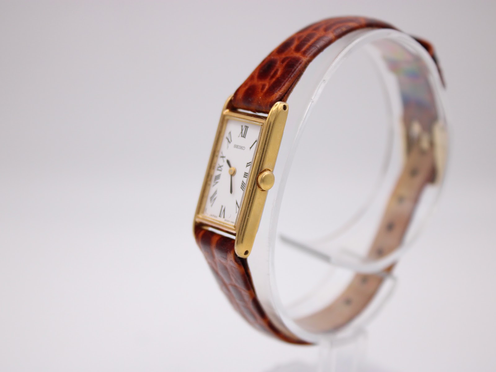Angled view of the Seiko 2E20-6120, highlighting the slim gold-plated case and brown crocodile-embossed leather strap on a display stand.