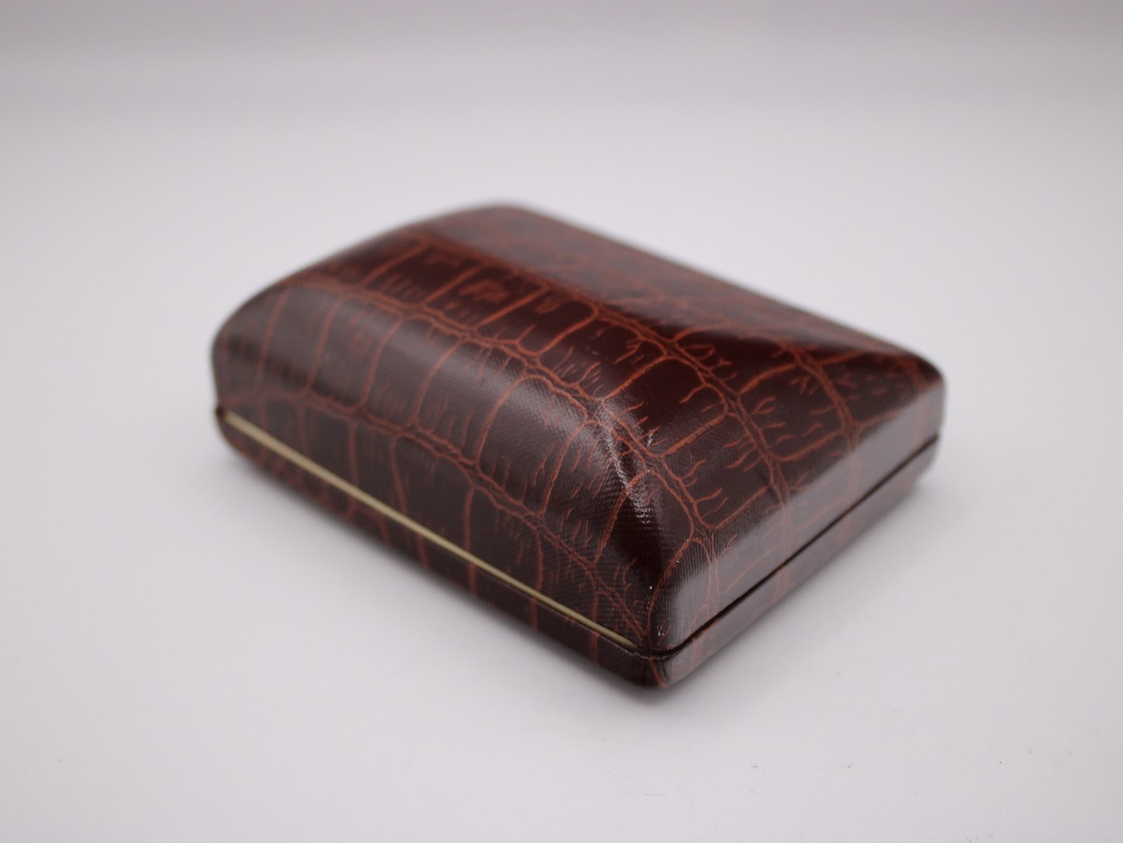 Top view of the closed original brown faux-crocodile watch box, featuring a gold trim.
