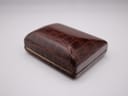 Top view of the closed original brown faux-crocodile watch box, featuring a gold trim.