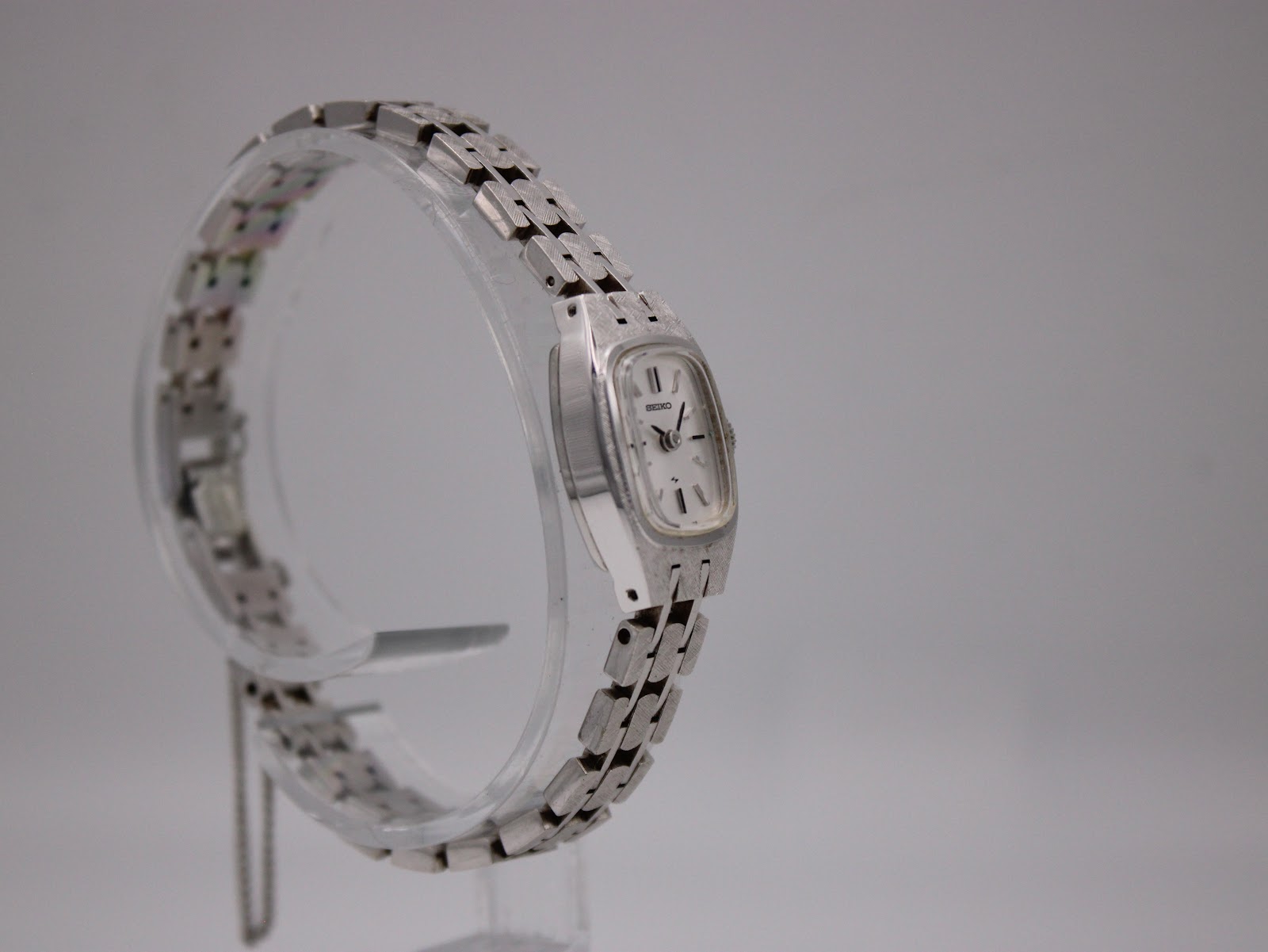 Angled view of the Seiko 2N0372 watch on a clear stand, showing the profile of the case and the integrated metal bracelet.