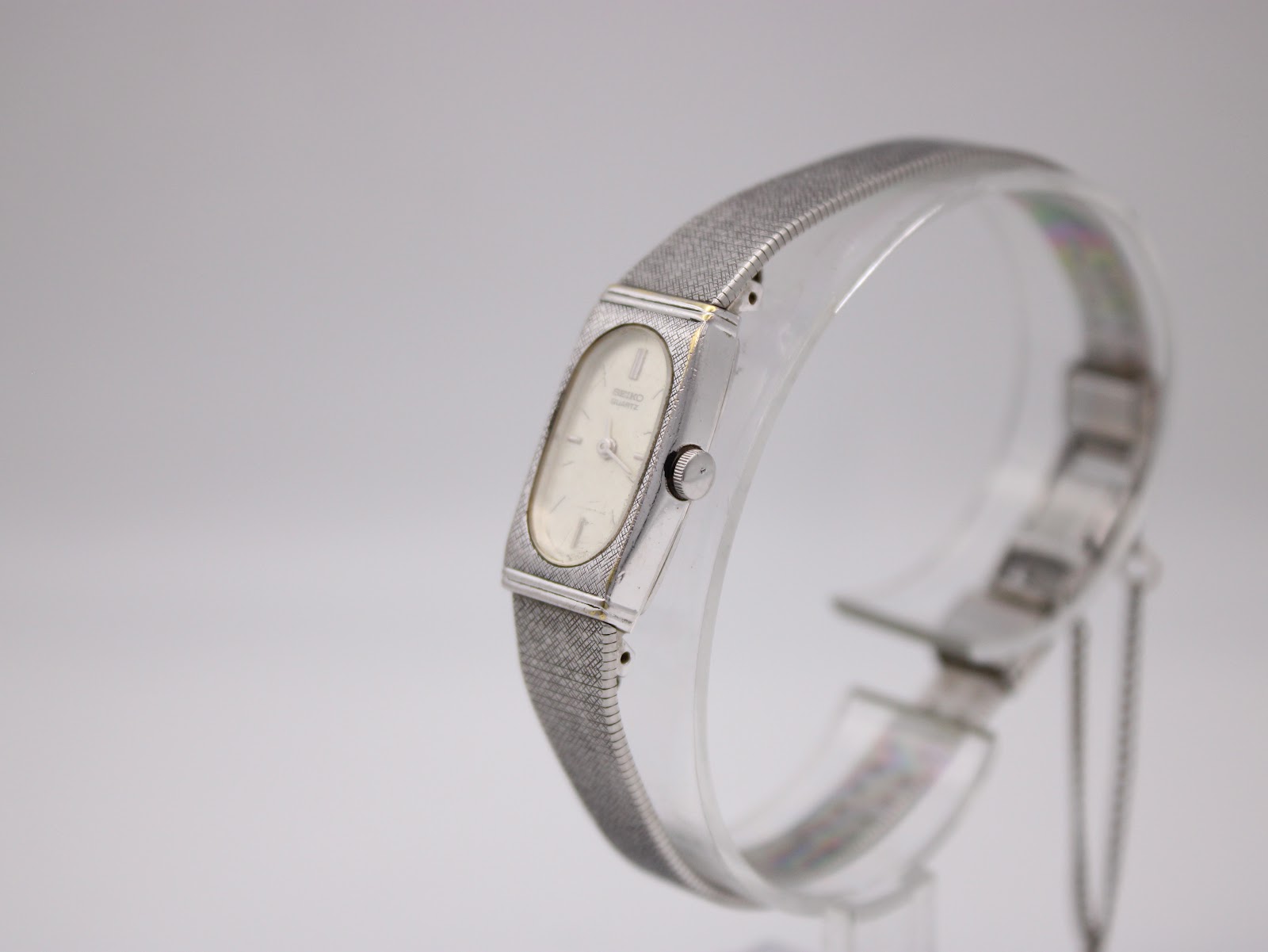 Angled side view of the Seiko watch, showing the crown and the curve of the mesh bracelet on the display stand.