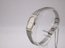 Angled side view of the Seiko watch, showing the crown and the curve of the mesh bracelet on the display stand.
