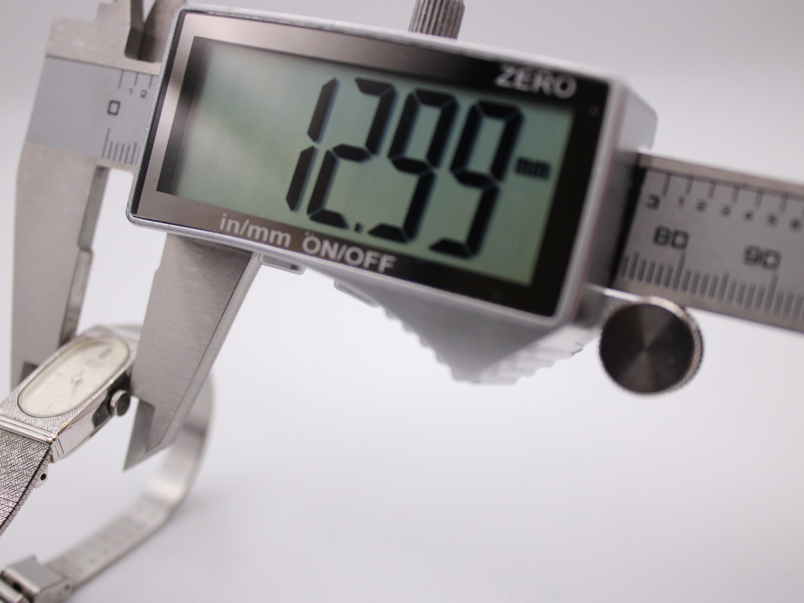Digital caliper measuring the case width of the Seiko watch, displaying a precise measurement of 12.99mm.