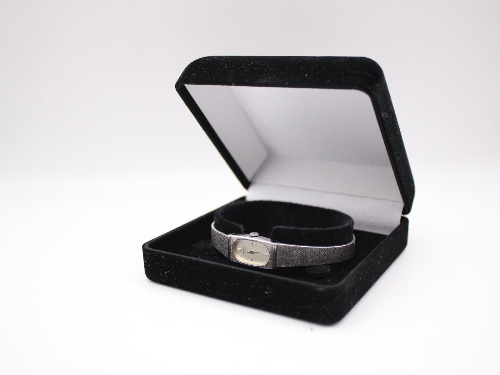 The Seiko watch nestled inside an open black velvet watch box.