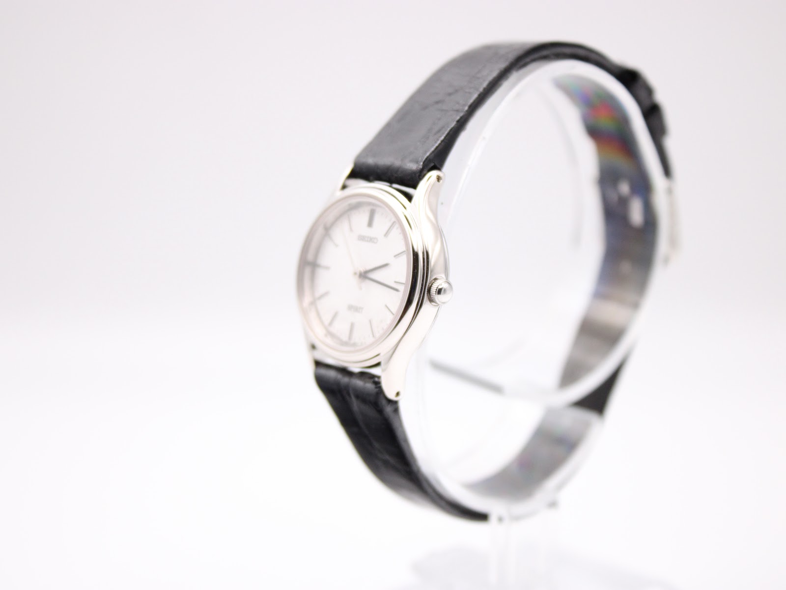 Front view of the Seiko Spirit watch on a stand, showing its round silver case, white dial, and black leather strap.