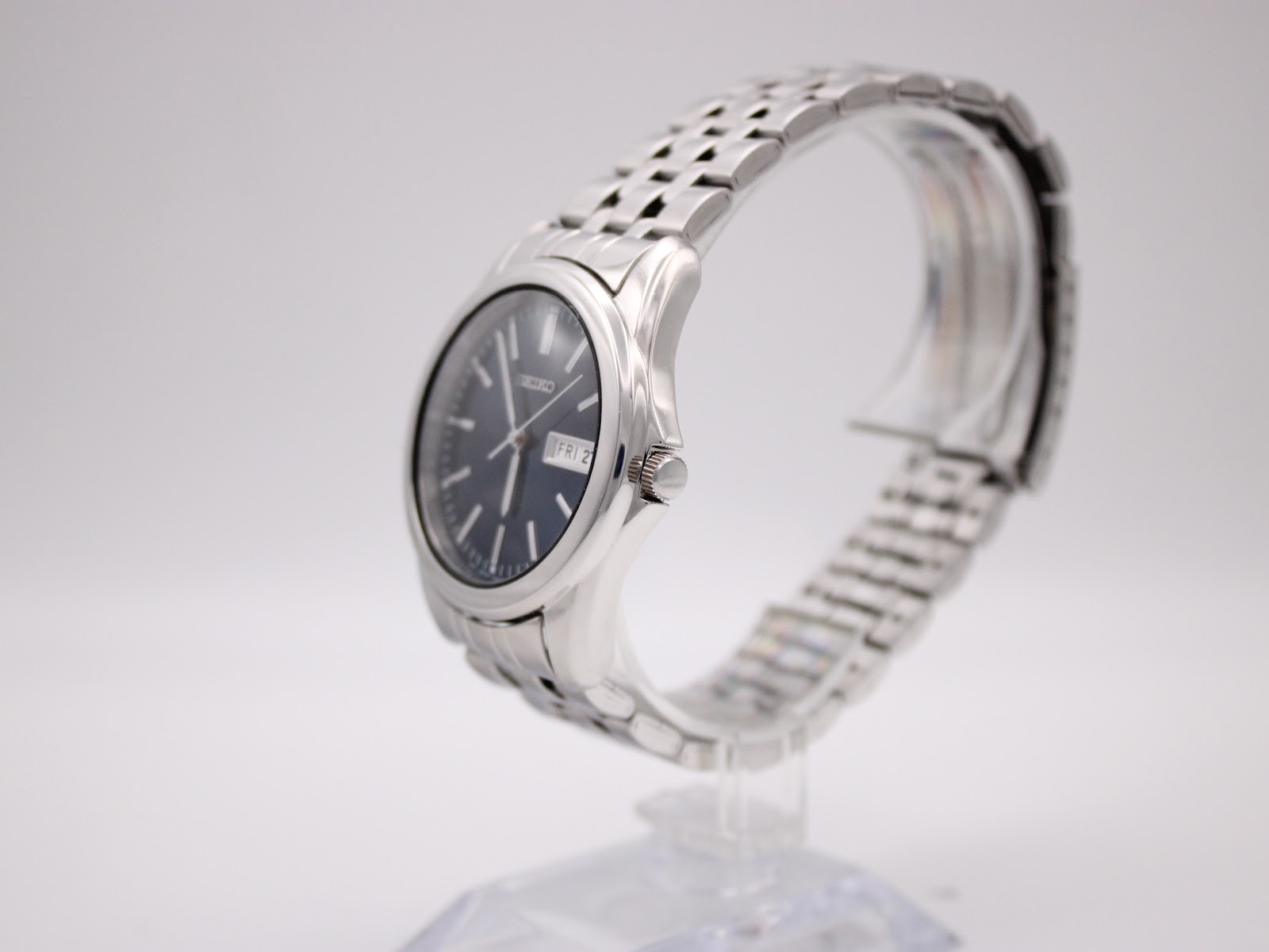 Side profile of Seiko 7N43-0AM0 showing round stainless steel case, polished bezel, and integrated five-link bracelet on a stand