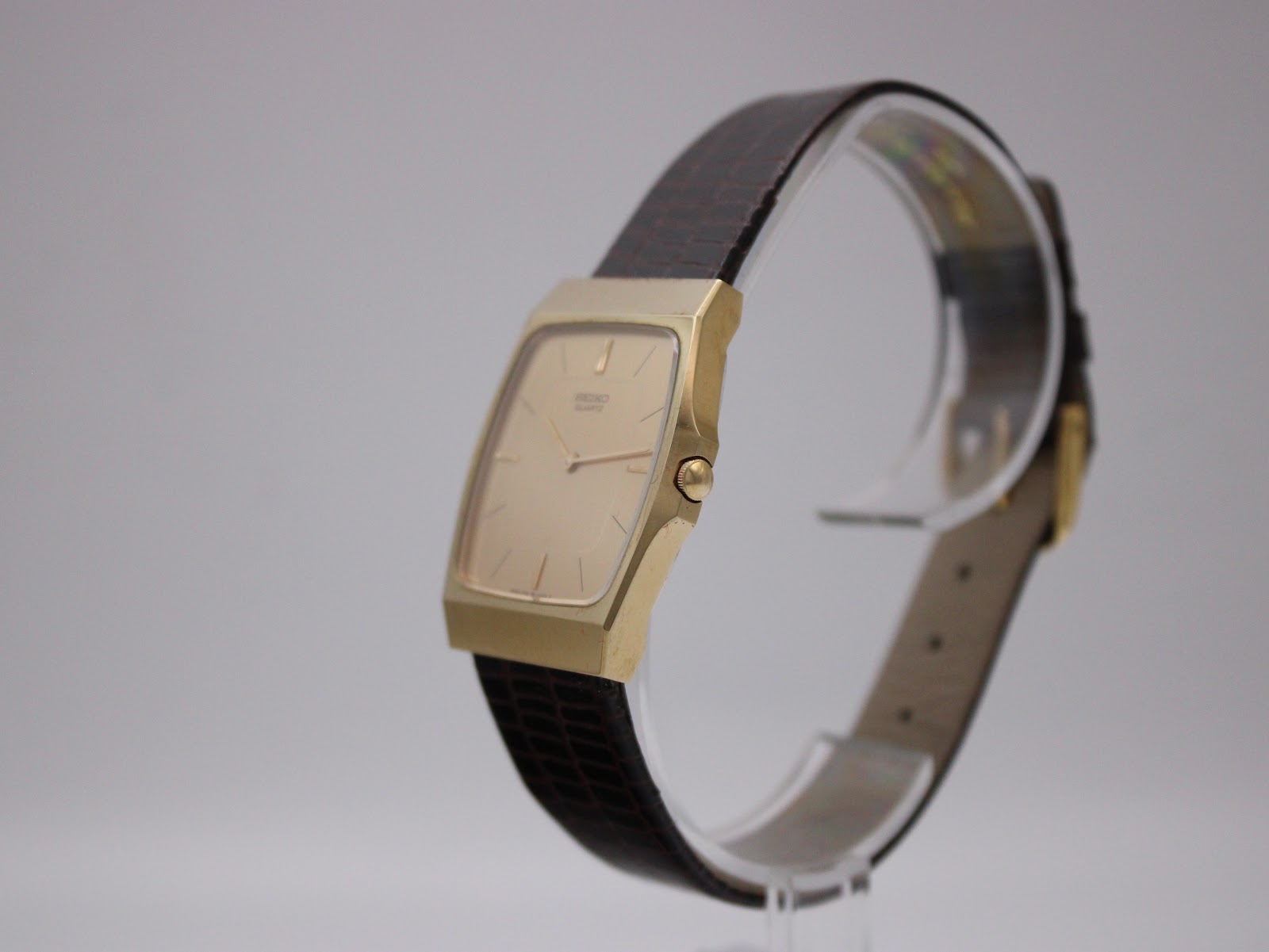 Angled side view of the Seiko gold-tone watch, showing the case profile and burgundy leather strap.