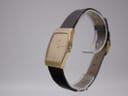 Angled side view of the Seiko gold-tone watch, showing the case profile and burgundy leather strap.