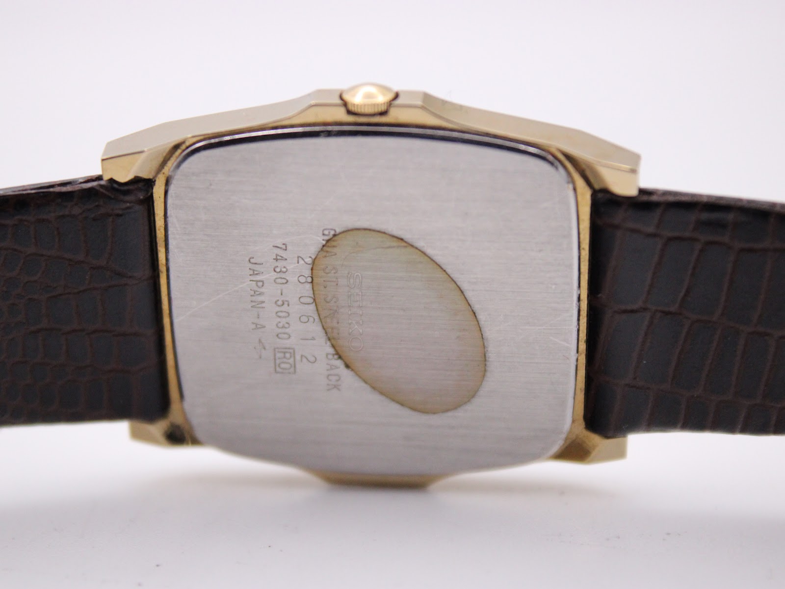 Close-up of the stainless steel case back of the Seiko watch, showing engravings 'SEIKO G.M. ST. STEEL BACK 280612 7430-5030 JAPAN-A' and some discolouration.