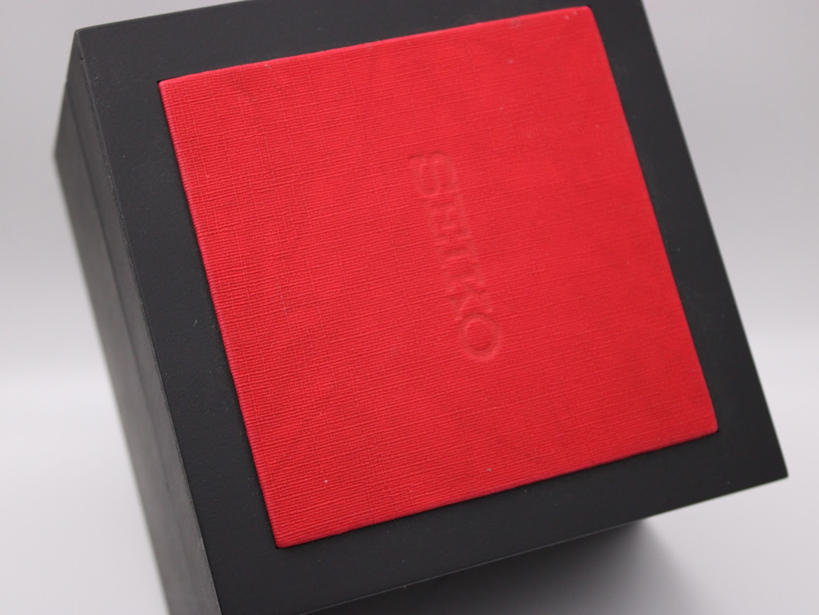 Close-up of the top of the black original Seiko watch box, showing an embossed Seiko logo on the red interior cushion.