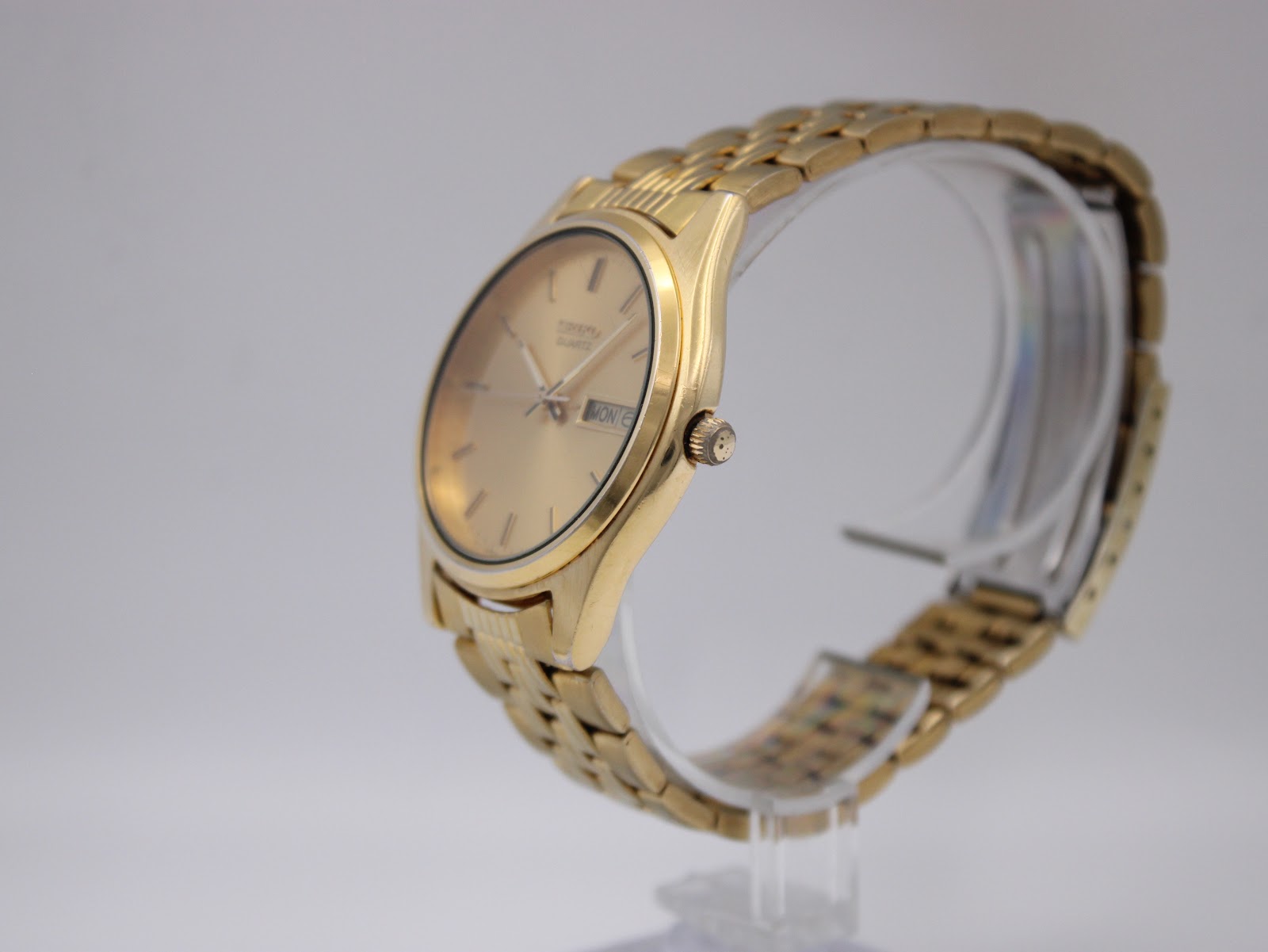 Angled side view of the Seiko watch on a clear stand, showing the crown and integrated bracelet.