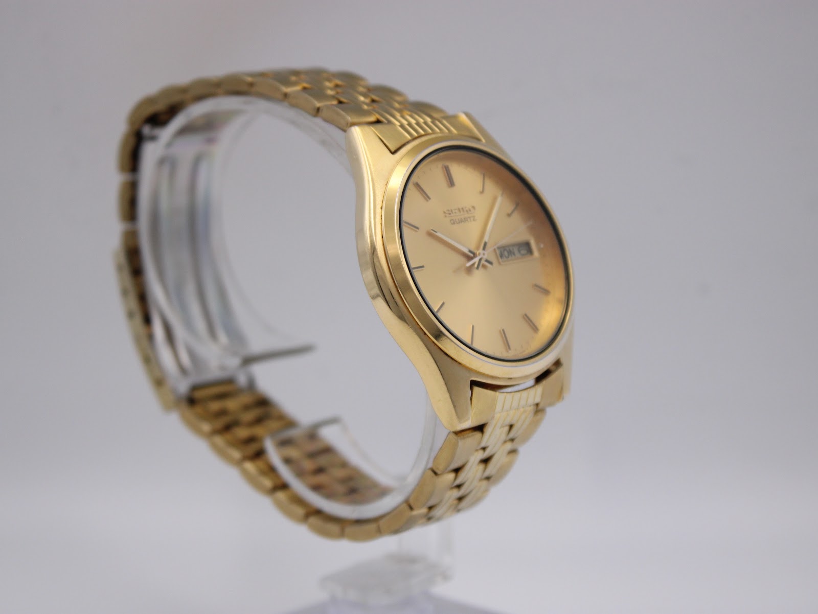 Opposite angled side view of the gold-tone Seiko 7N43-9011 watch on a stand, highlighting the case and bracelet.