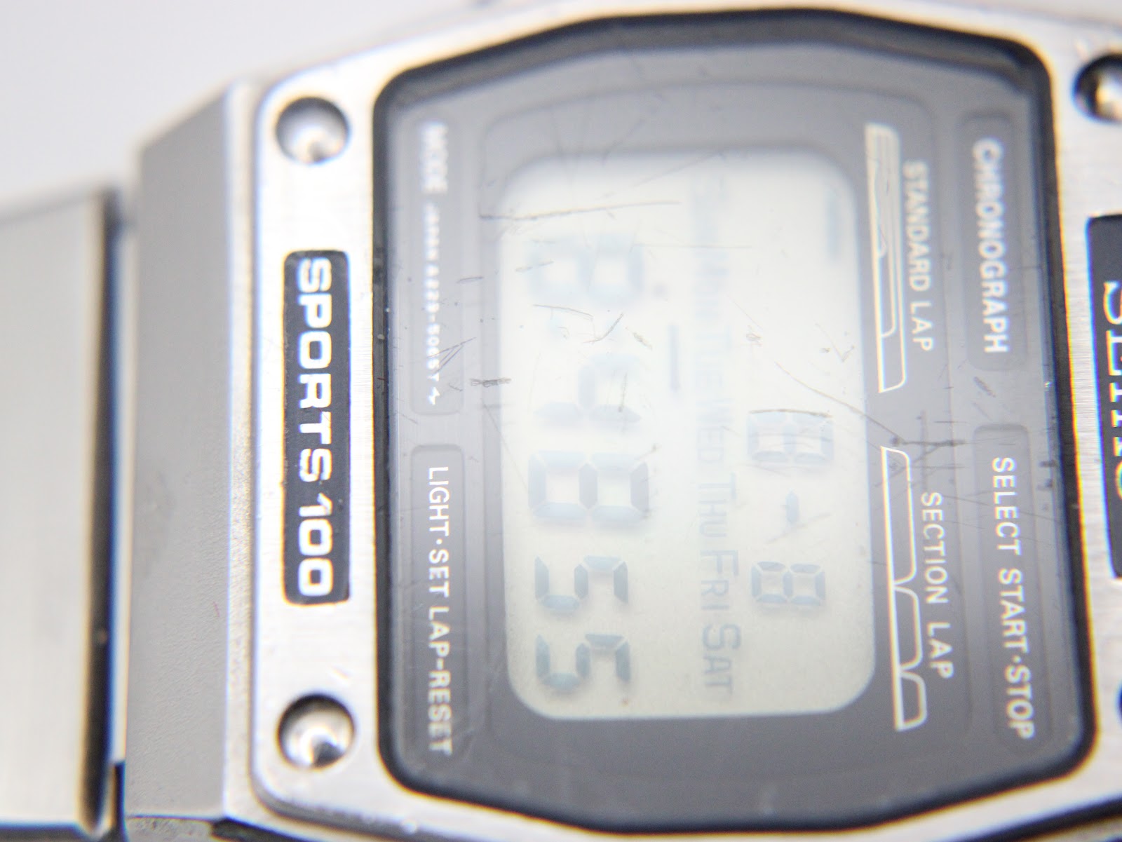 Extreme close-up of the digital LCD display and acrylic crystal, showing visible surface scratches on the crystal.