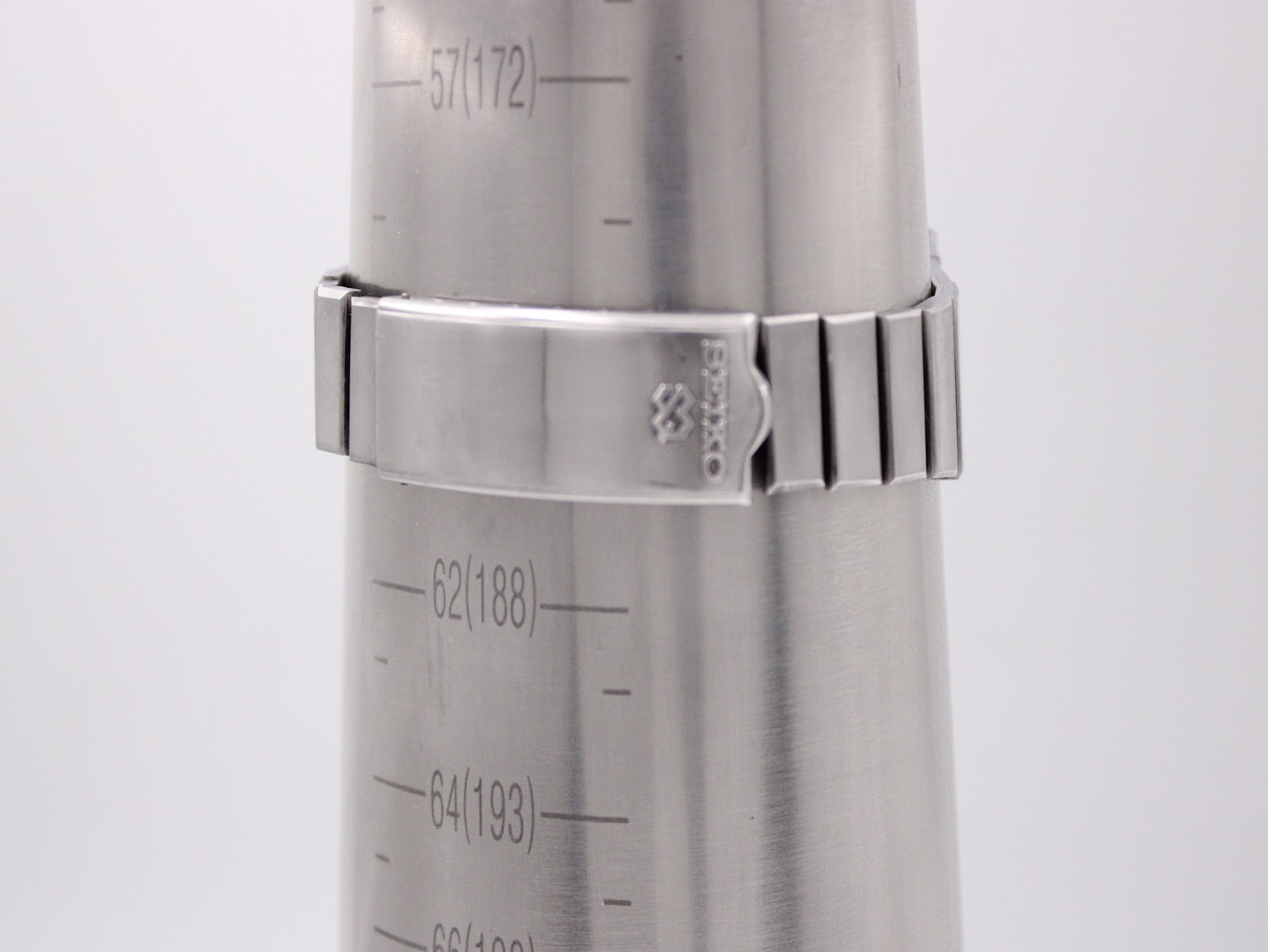 Close-up of the integrated stainless steel bracelet and signed Seiko clasp on a wrist sizing cone, indicating an approximate wrist size.