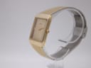 Side profile view of the gold tone Seiko watch on a clear stand, showing the textured crown.