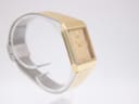 Angled side view of the gold tone Seiko watch on a clear stand, highlighting its slim rectangular case.