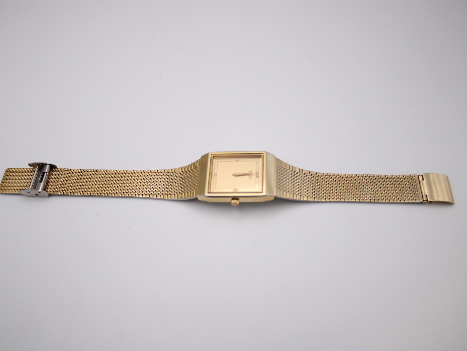 Top-down view of the entire gold tone Seiko watch with its integrated mesh bracelet laid flat.