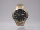 Front view of gold tone Seiko watch with black dial and gold baton indices on a white background.
