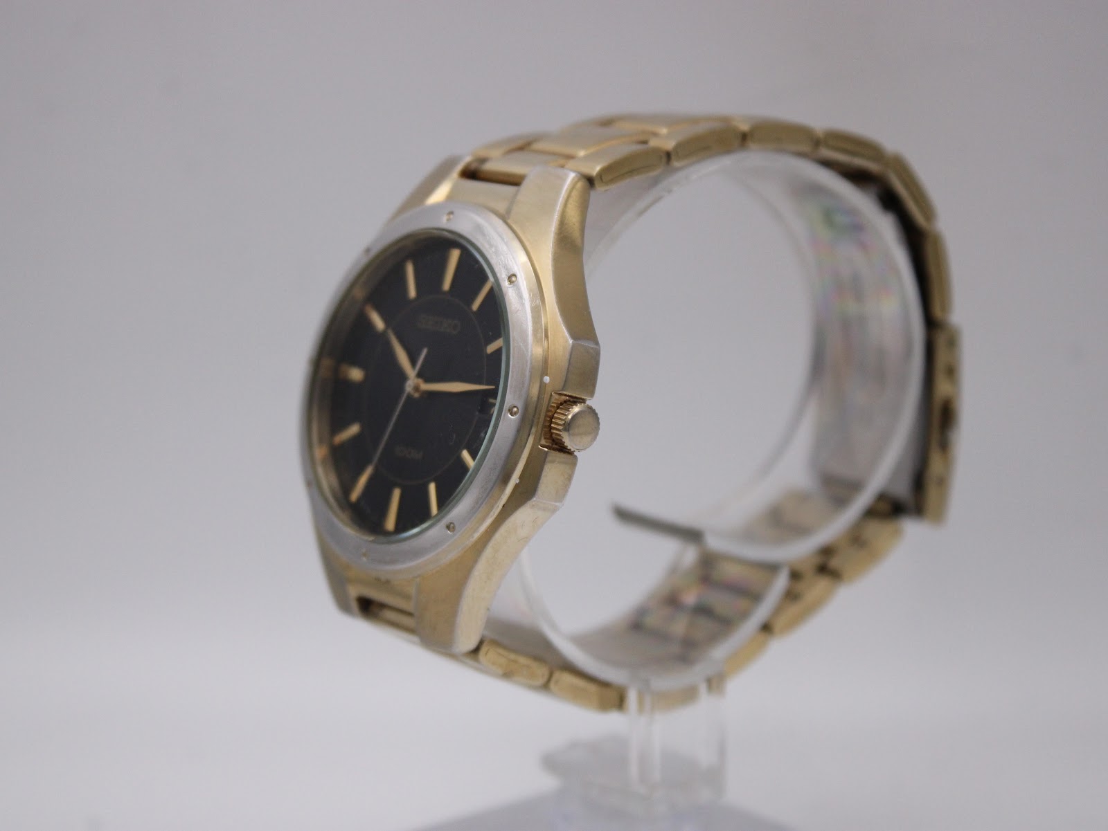 Angled side view of the Seiko watch, showing the gold tone case, crown, and integrated bracelet.