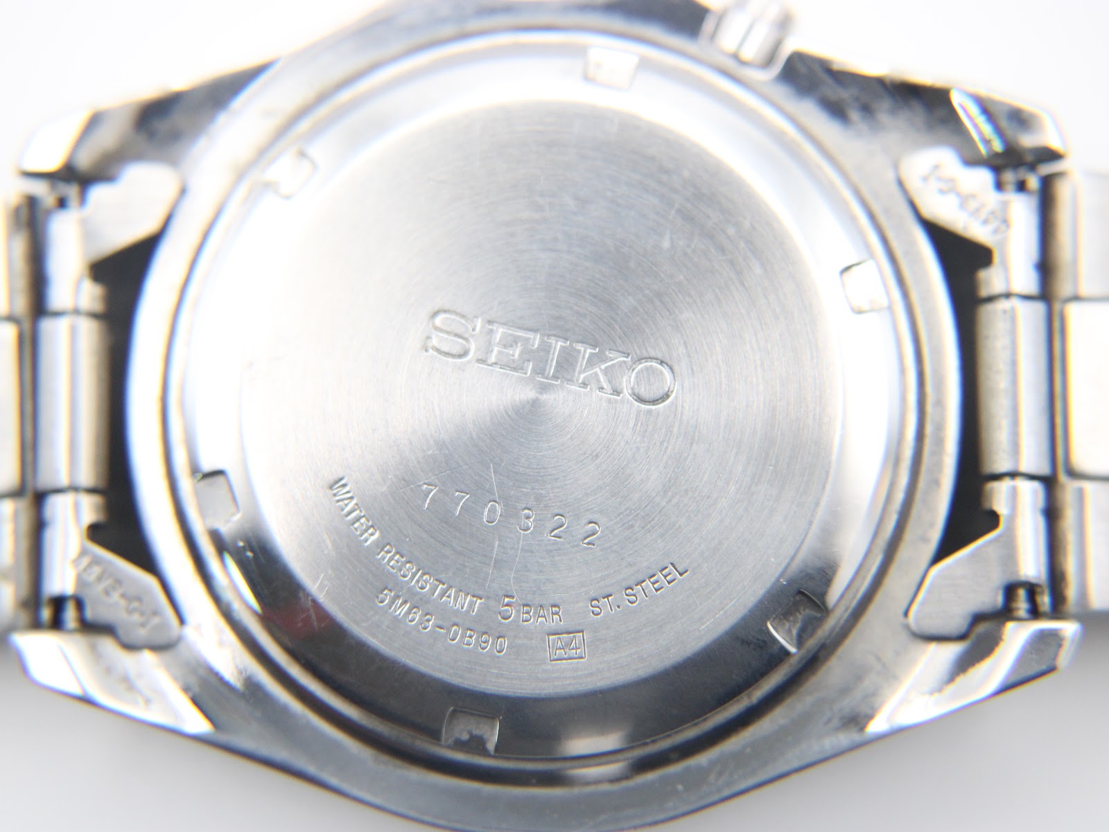 Close-up of the watch's stainless steel case back, displaying "SEIKO", serial number 770322, model 5M63-0B90, and water resistance details.