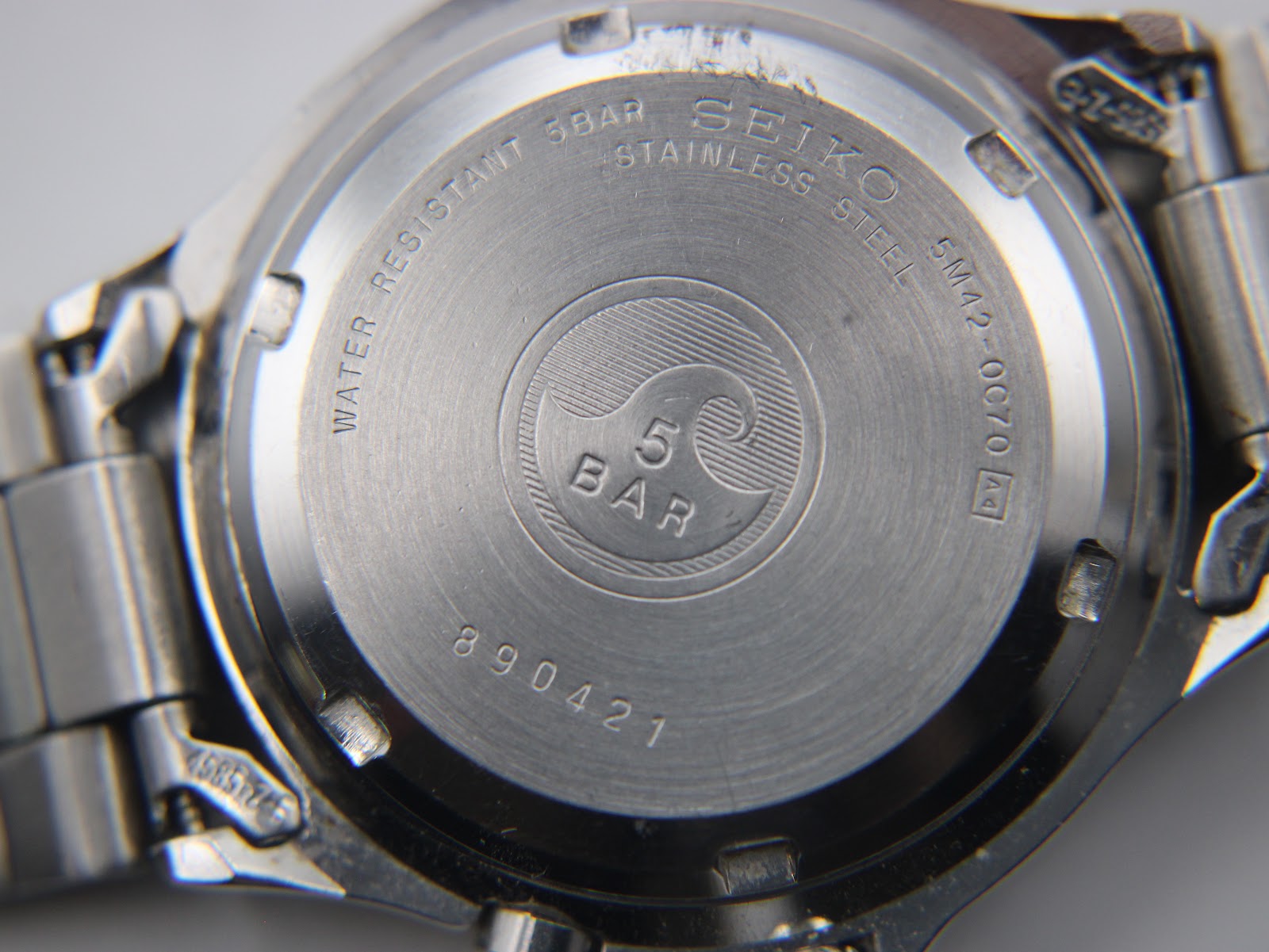 Close-up of stainless steel case back with Seiko branding, 5 bar water resistance, model number 5M42-0070, and serial number.