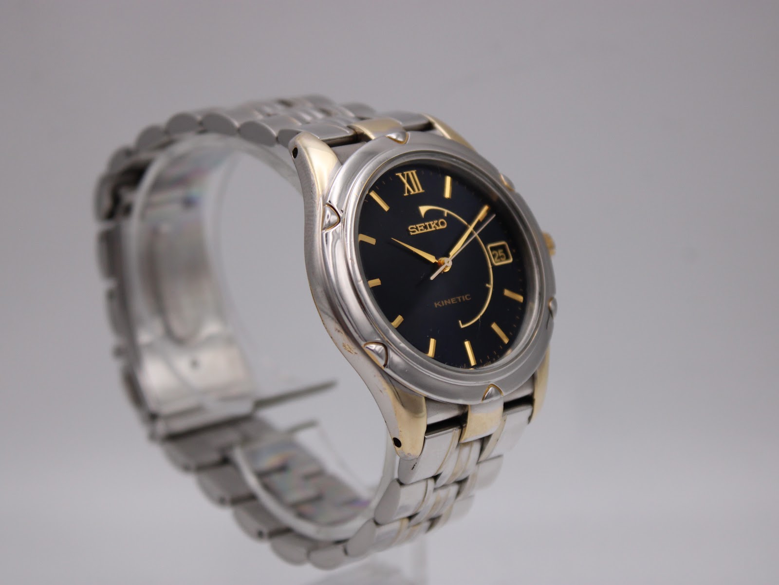 Angled right view of the Seiko Kinetic watch on a display stand, showing the case profile, gold crown, and pusher.
