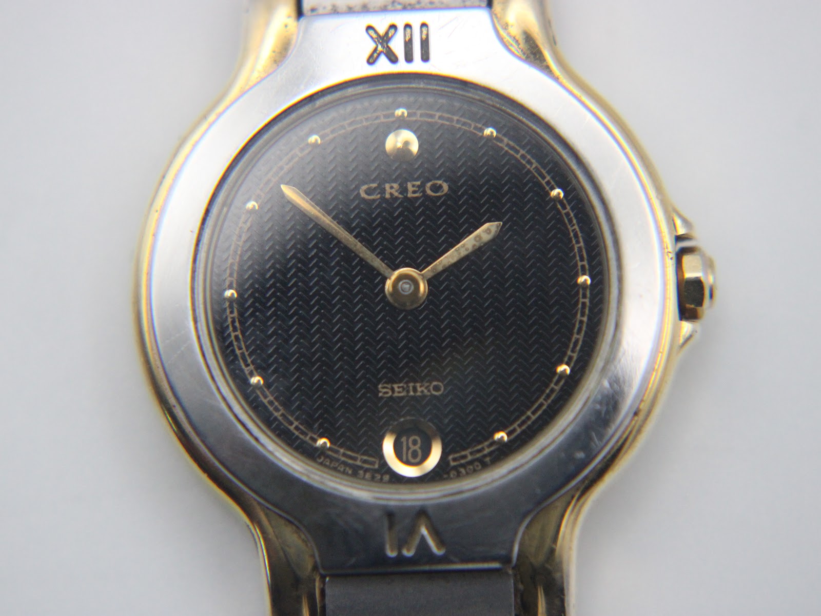 Detailed close-up of the Seiko Creo black textured dial, showing gold-tone Roman numerals, dot indices, and date window.
