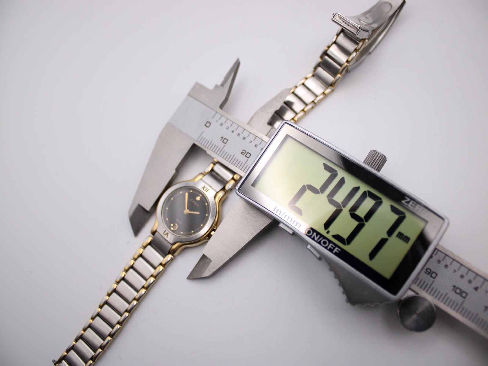 Overhead view of the Seiko watch being measured by a digital caliper, displaying a case diameter of 24.97mm.