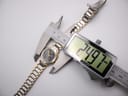 Overhead view of the Seiko watch being measured by a digital caliper, displaying a case diameter of 24.97mm.