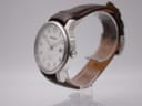 Side view of the Seiko watch, showing the polished stainless steel case, crown, and brown leather strap on a clear stand.