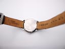 Interior view of the brown leather strap, showing 'NIK CHARM' and 'GENUINE LEATHER 20' markings, with the case back in the centre.