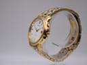 Angled side view of the gold-tone Seiko kinetic watch on a clear display stand, showing the case profile and crown.