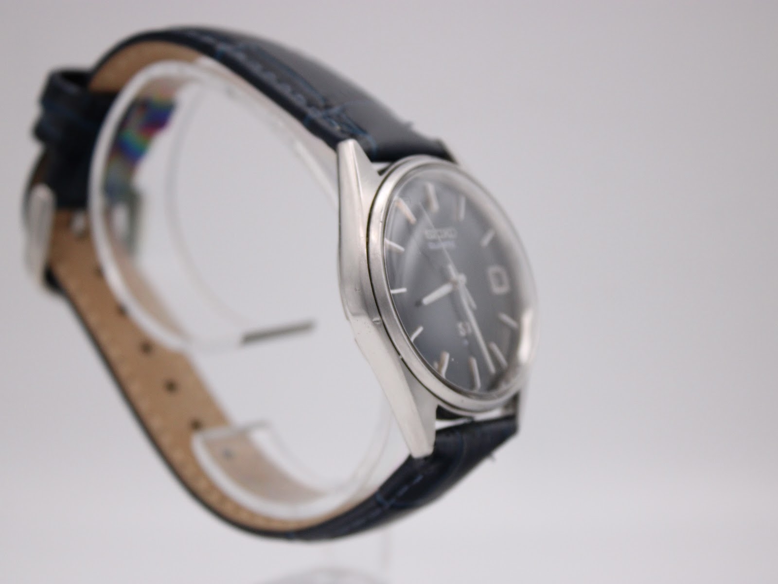 Close-up view of the watch's deep navy blue dial, silver baton indices, and date window.