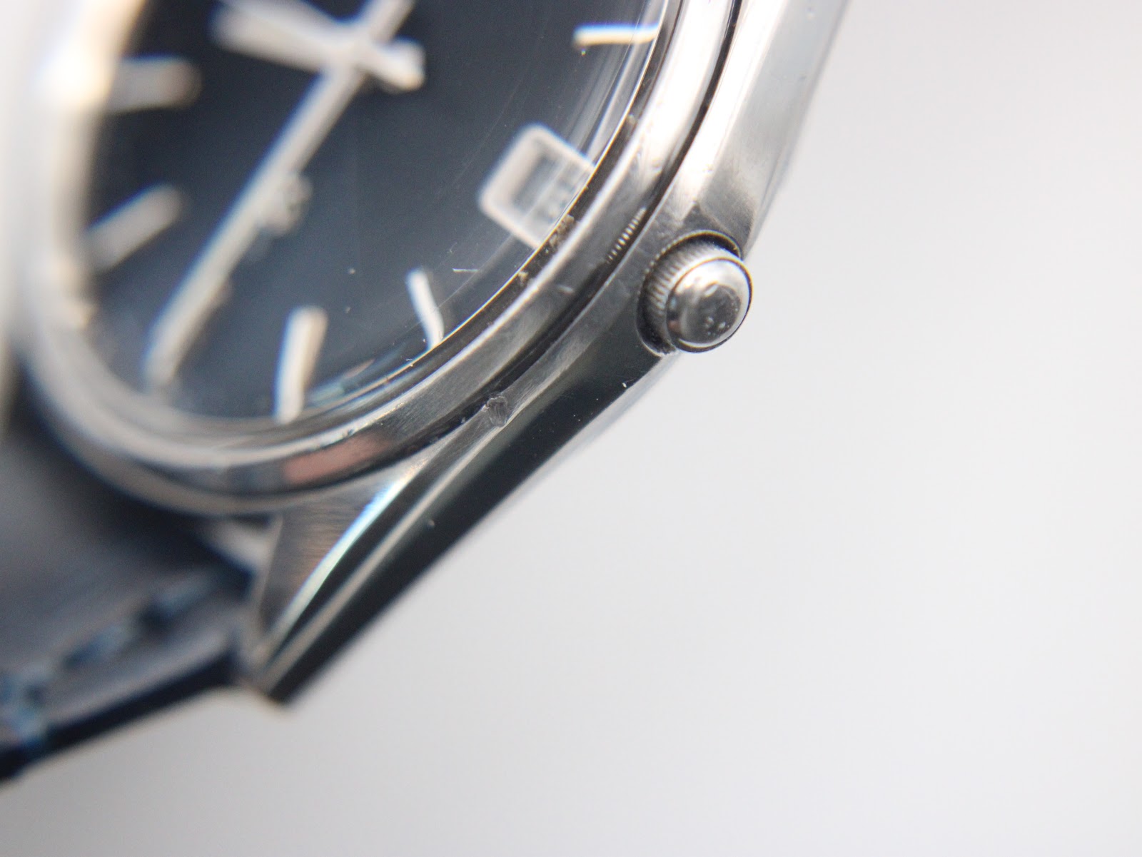 Detail shot of the polished stainless steel case lugs and the textured navy blue leather strap.