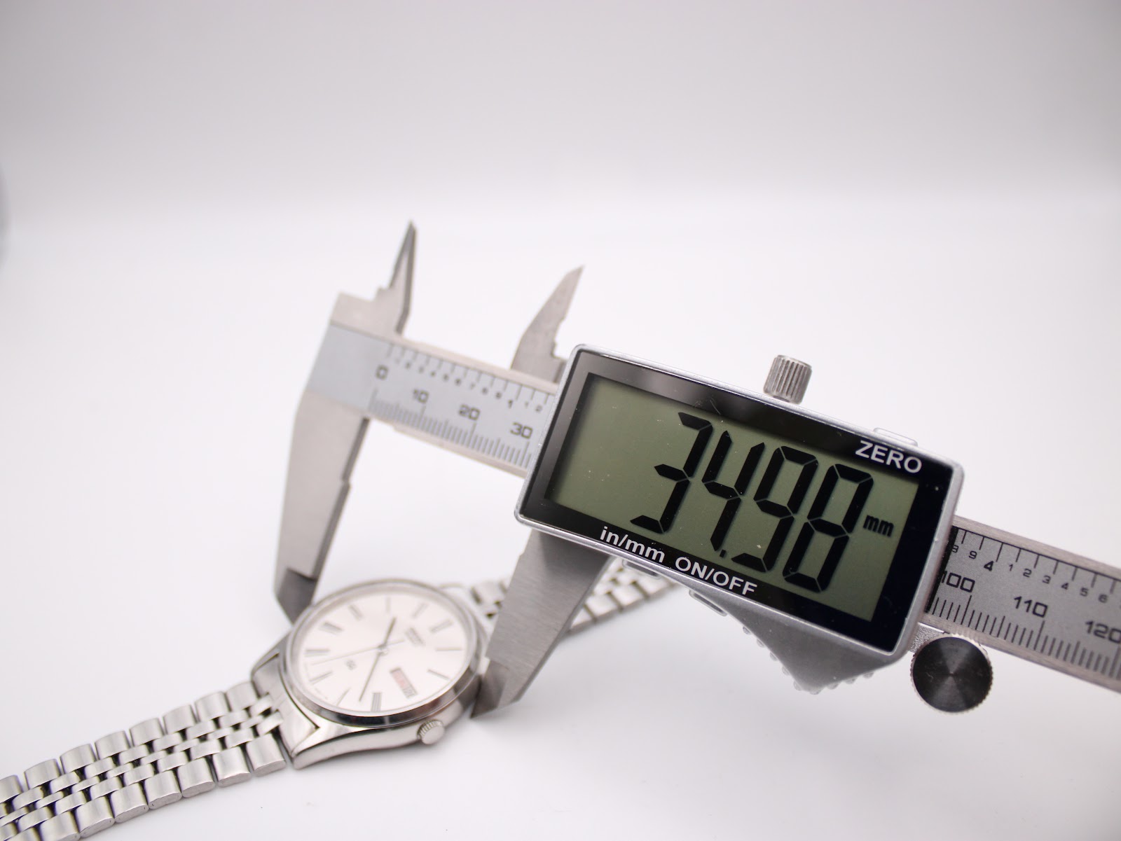 Digital caliper measuring the case diameter of the Seiko watch, displaying a precise measurement of 34.98mm