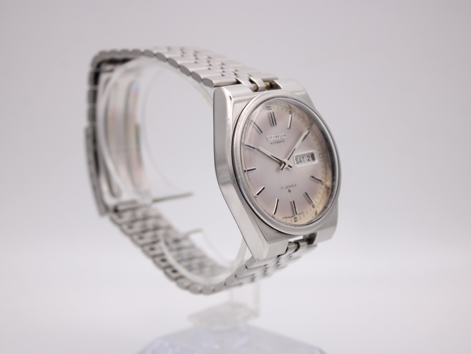 Angled left side view of the vintage SEIKO watch on a clear display stand, showing the crown and integrated bracelet.