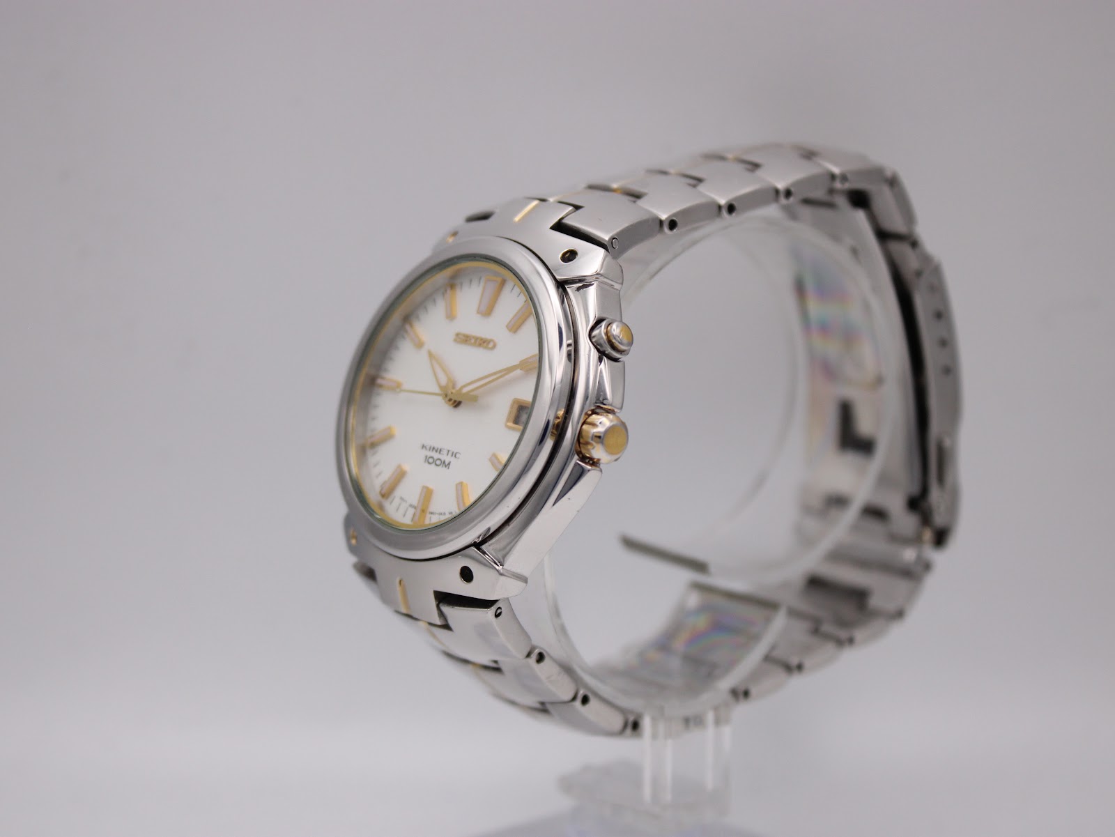 Angled side view of the Seiko watch on a stand, showing the gold-tone crown and pusher.