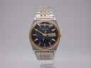 Front view of Seiko V743-9020 two-tone watch with navy dial, gold baton indices, and day-date window.