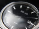 Close-up of the watch's black sunburst dial showing applied indices and visible crystal scratches.