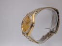 Side profile of the Seiko gold-tone watch on a clear display stand, highlighting the case shape and crown.