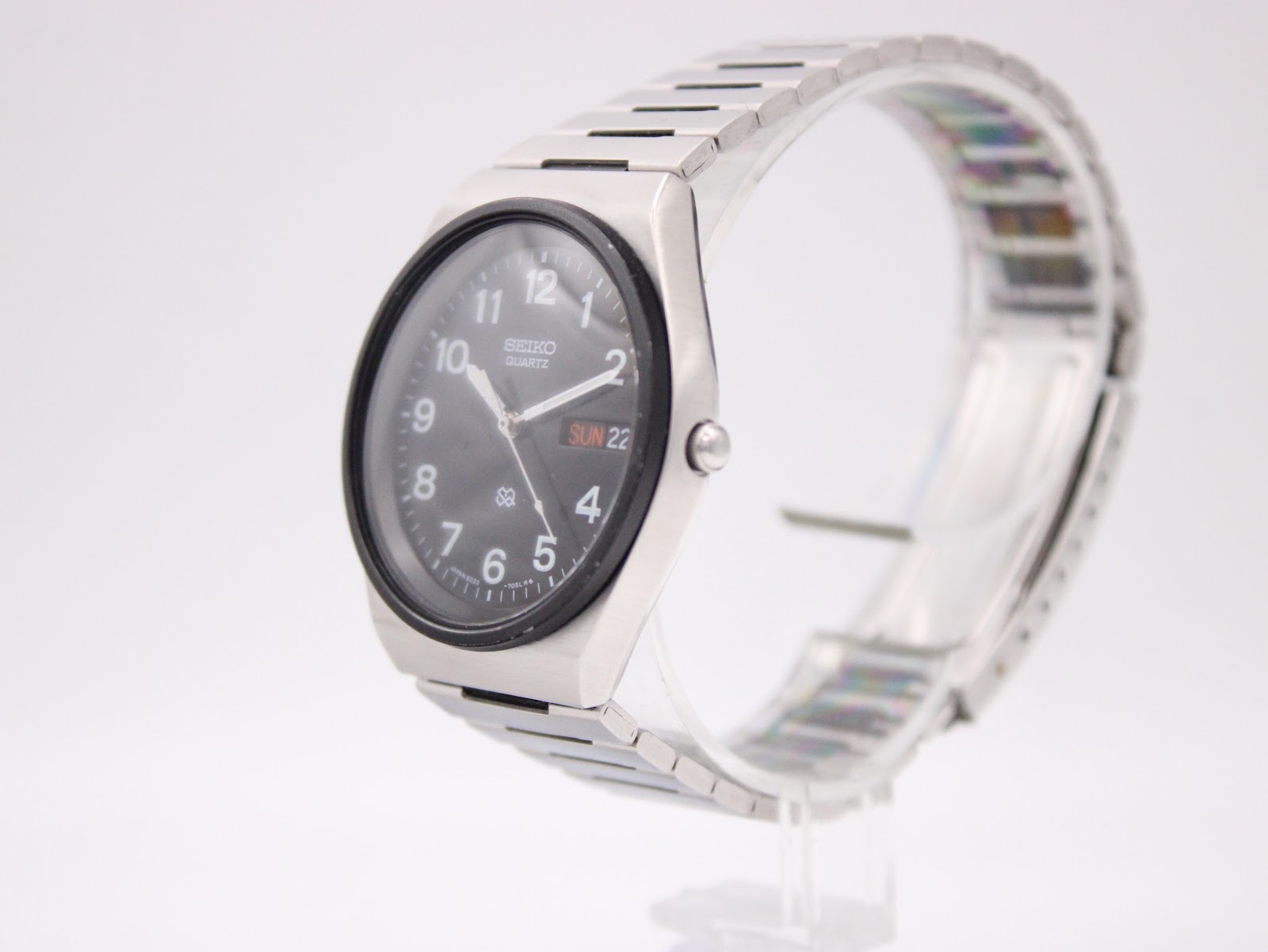 Angled side view of the Seiko watch on a clear stand, showcasing its tonneau-shaped case and integrated steel bracelet.