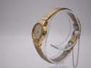 Side profile view of the gold-tone Seiko watch on a clear stand, showing the case and textured mesh bracelet.